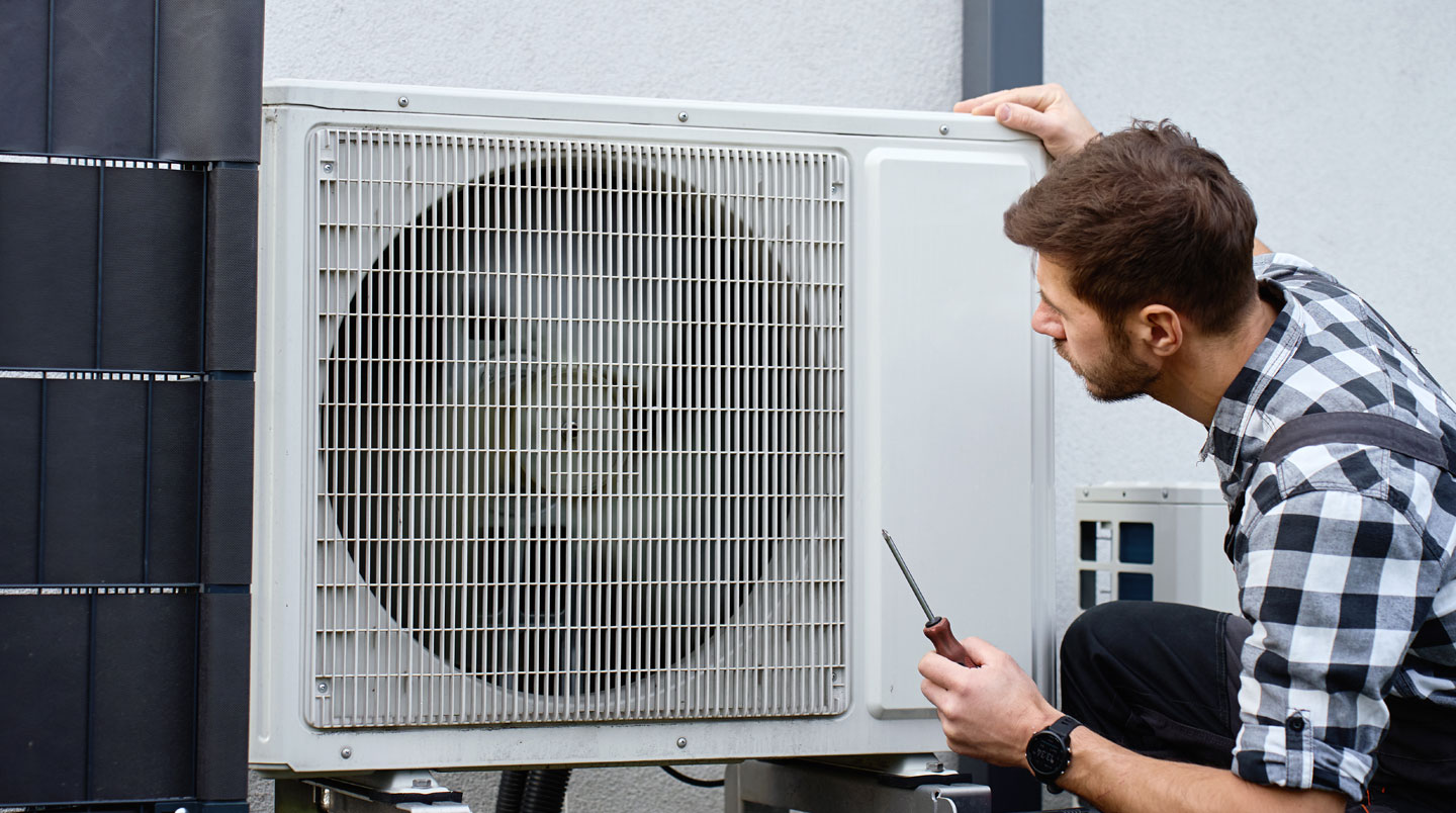 Technicien CVC effectuant l'entretien préventif d'une thermopompe murale en retirant le filtre à air de l'unité intérieure dans un intérieur résidentiel québécois